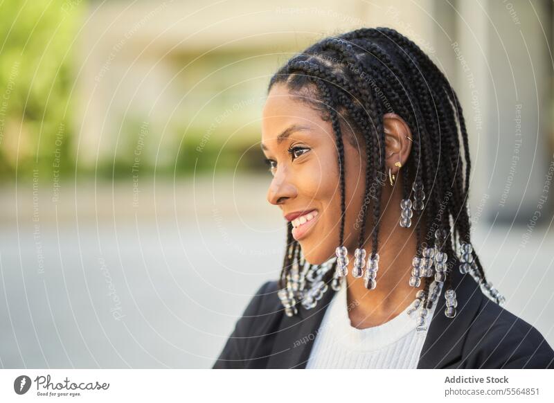 Lächelnde stilvolle afroamerikanische Frau vor einem unscharfen Hintergrund Stil Geschäftsfrau selbstbewusst Outfit Gebäude urban modern positiv Unternehmer