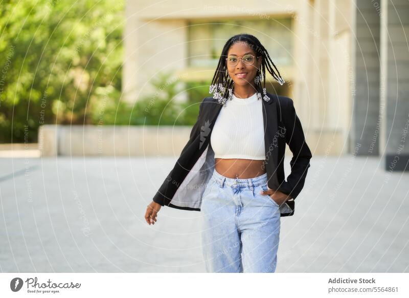 Lächelnde stilvolle afroamerikanische Frau vor einem unscharfen Hintergrund Stil Geschäftsfrau selbstbewusst Outfit Gebäude urban modern positiv Unternehmer