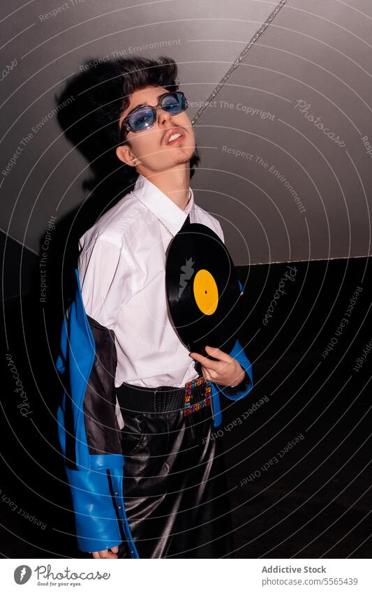 Mann im Retro-Look mit Schallplatte im Dunkeln stylisch Brille faulenzen Vinyl Aufzeichnen blau Jacke Leder Hose dunkel retro Musik Mode Stil 80s Ambiente