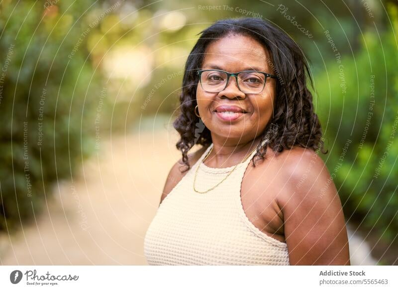 Strahlende Frau genießt die Schönheit der Natur Garten Lächeln krause Haare Porträt Afroamerikaner im Freien Sommer Tag Freude Mode Baum heiter Emotion grün