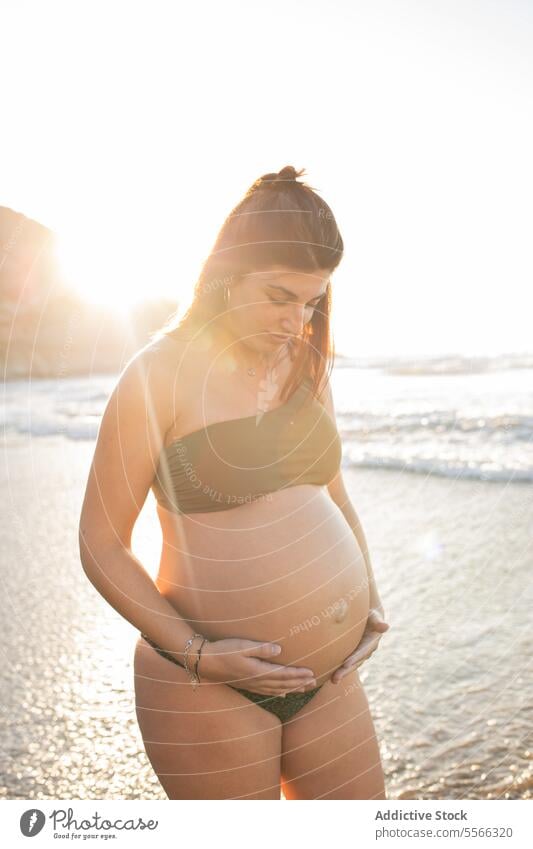 Schwangere Frau im Meerwasser stehend schwanger Bauch erwarten MEER Bikini Sommer Sonnenuntergang berühren Glück heiter Lächeln pränatal vorwegnehmen