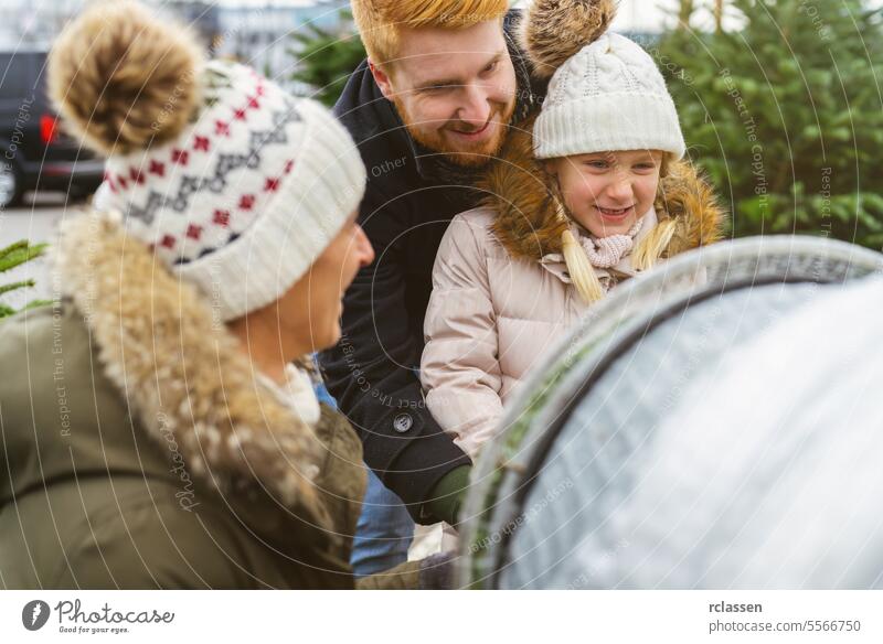 Eine Familie wickelt auf einem Straßenmarkt einen gefällten, in ein Plastiknetz verpackten Weihnachtsbaum ein Teamwork kaufen Hilfsbereitschaft Kind Tochter