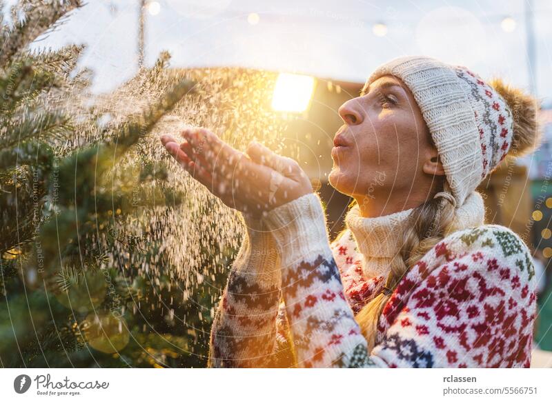 Beauty Winter Girl Blowing Snow auf ihrem ausgewählten Weihnachtsbaum auf einem Weihnachtsbaummarkt. Kauf Bauernhof Kiefer Norwegen Fairness Markt Werkstatt