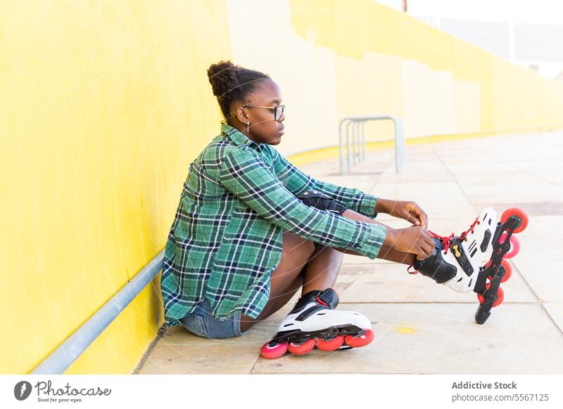 Frau mit Rollschuh an der gelben Wand im Skatepark Rolle Schlittschuh Schuh befestigen Vorbereitung lässig Skateplatz Sport sitzen Freizeit Wochenende Aktivität