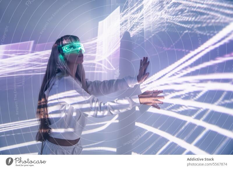 Frau in VR-Brille berührt Wand mit Lichtern berühren futuristisch erkunden Cyberspace Studioaufnahme sich[Dat] einbilden lange Haare Pony trendy Stil blond