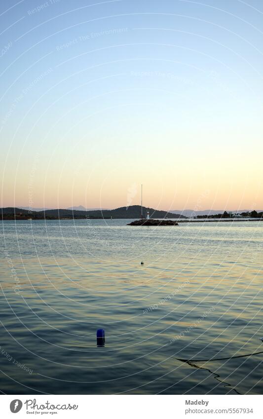 Romantische Abendstimmung am Meer mit dem Licht der Abendsonne mit Leuchtturm und Pier am Hafen in der Bucht von Ayvalik am Ägäischen Meer in der Provinz Balikesir in der Türkei