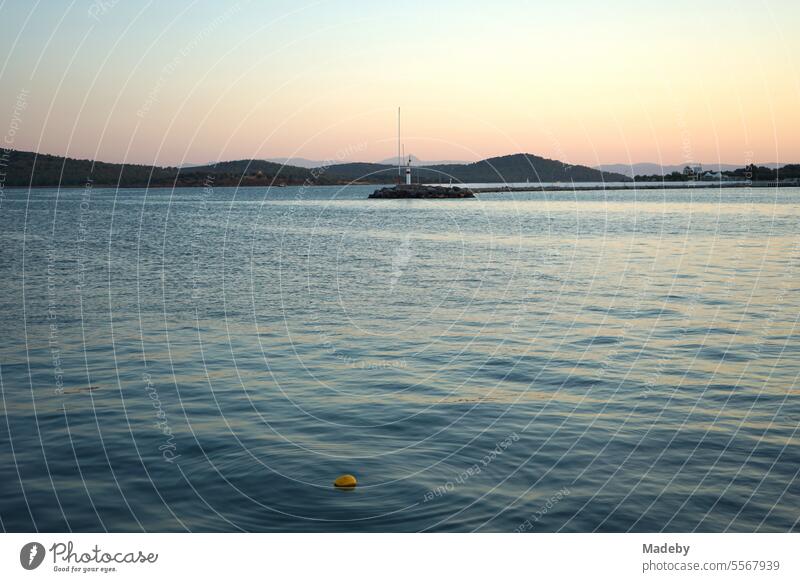 Romantische Abendstimmung am Meer mit dem Licht der Abendsonne mit Leuchtturm und Pier am Hafen in der Bucht von Ayvalik am Ägäischen Meer in der Provinz Balikesir in der Türkei