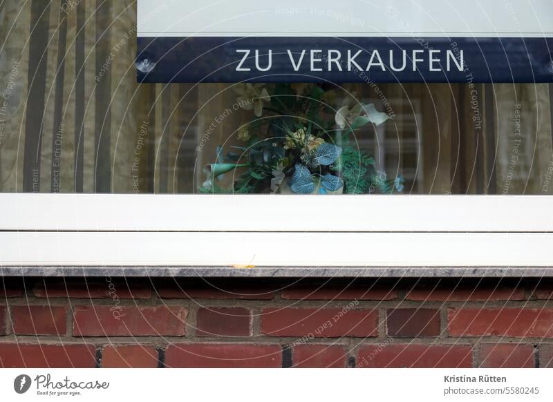 zu verkaufen steht am fenster mit dem plastikblumengesteck schild wohnung haus gardine kunstblumen zuhause wohnen leben immobilie wohnungsmarkt immobilienmarkt