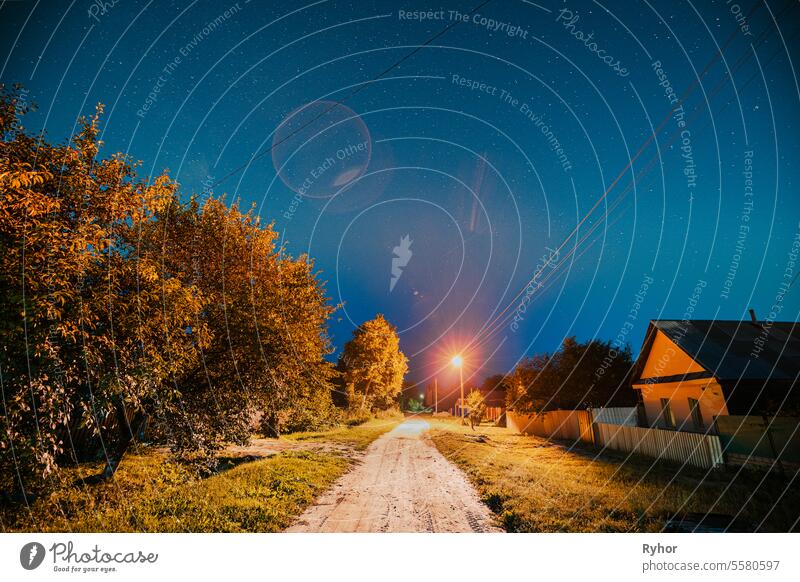 Nachthimmel über Straße mit Häusern im Dorf. Nacht Sternenhimmel über dem Dorf mit hellen Sternen und meteorologischen Spur Spur. Glühende Sterne über Sommer Natur