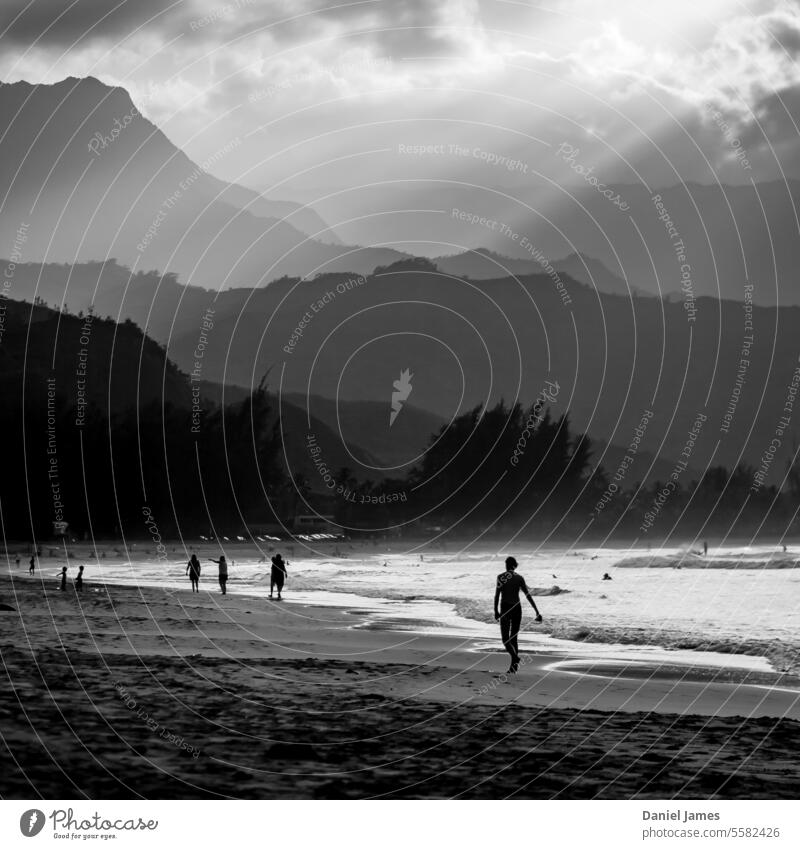 Nachmittagsspaziergang an einem hawaiianischen Strand mit Sonnenlicht, das durch die Wolken bricht. Menschen Wasser Meer laufen schlendernd Berge u. Gebirge