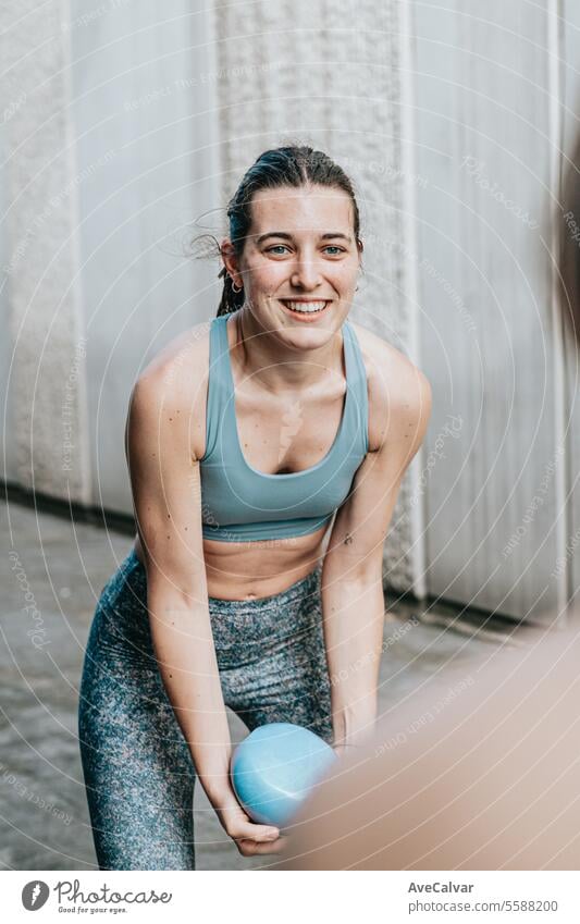 Lächelndes sportliches Mädchen bei einer Reihe von Übungen mit einem Medizinball am Trainingstag. Urbane Szene. Fitness Gesundheit Frauen Lifestyle Sport