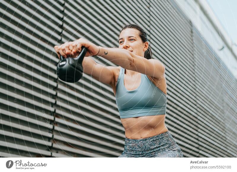 Junge Frau macht Kniebeugen mit Gewicht. Urbane außerhäusliche Umgebung, Sportbekleidung und gesundes Leben. Fitness sportlich im Freien urban Freunde Training