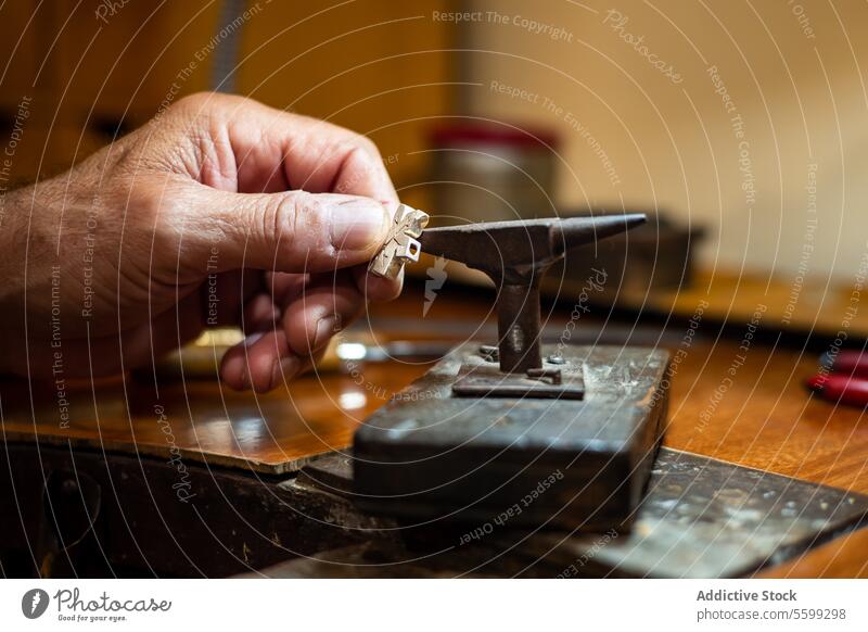 Goldschmied beim Herstellen und Reparieren von Goldschmuck in seiner Werkstatt mit einem Amboss. Juwelier bei der Arbeit an einem Silberschmuckstück. Klette