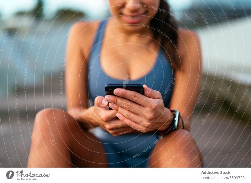 Lächelnde lateinamerikanische Frau, die nach dem Training im Freien ihr Smartphone benutzt Lateinamerikaner Technik & Technologie Sitzen Pause Übung heiter