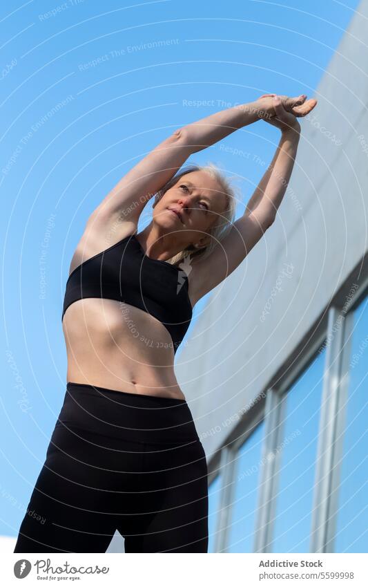 Aktive ältere Frau, die sich unter klarem blauen Himmel im Freien dehnt Fitness Übung strecken Gesundheit Wellness aktiv Blauer Himmel sportlich Sportbekleidung