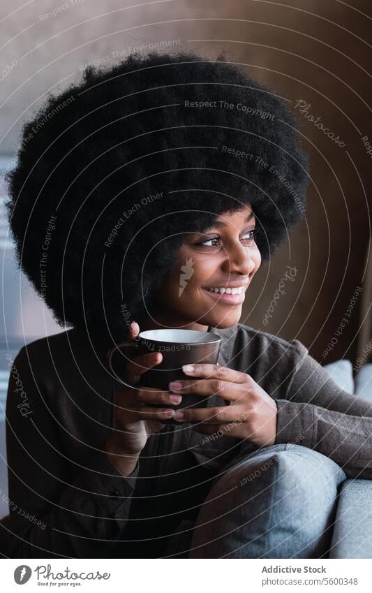 Fröhliche schwarze Frau mit einer Tasse Kaffee Heißgetränk Getränk Afro-Look Fenster Lächeln Freizeit Erfrischung Frisur feminin Vorschein Glück charmant