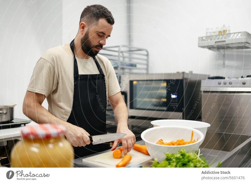 Junger Koch schneidet Karotten Küchenchef Essen zubereiten Lebensmittel professionell Restaurant Gemüse Messer Schneiden Mann jung Arbeit männlich Speise Person