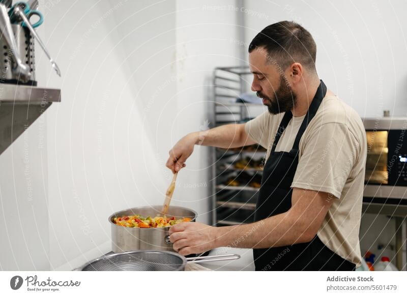 Junge Köchin beim Kochen mit einer Kasserolle Küchenchef Essen zubereiten Lebensmittel professionell Restaurant Gemüse Veganer Kichererbsen Mann jung Arbeit