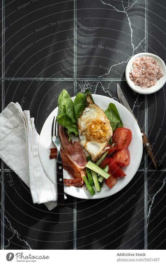 Ausgewogener Frühstücksteller Teller Gesundheit Gemüse Tomate Salatgurke Spinat Blatt gebraten Ei Speck Streifen weiß Murmel Hintergrund dunkel Serviette Gewebe