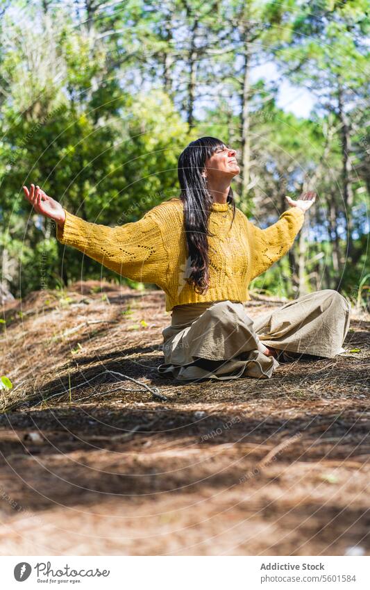 Frau, die mit ausgebreiteten Armen im Wald sitzt und in den Himmel schaut, als ob sie Gott danken würde. Vertikale Aufnahme. menschliche Hand Asana