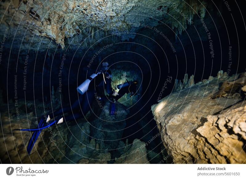 Anonyme Taucher schwimmen durch enge Gänge, umgeben von scharfen Stalaktiten und Stalagmiten in der Cenote Dos Ojos in Mexiko Durchgänge Tauchlampe glühen