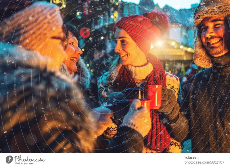 Fröhliche Freunde genießen Glühwein und heiße Schokolade auf einem verschneiten Weihnachtsmarkt Bowle Frohe Weihnachten Tasse Kakao Handschuhe traditionell