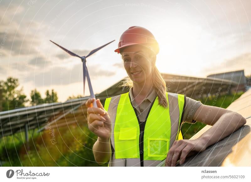 Weibliche Ingenieurin mit Windturbine Modell bei Solarenergie Farm Photovoltaik-Panel-System bei Sonnenuntergang. Alternative Energie ökologisches Konzept.