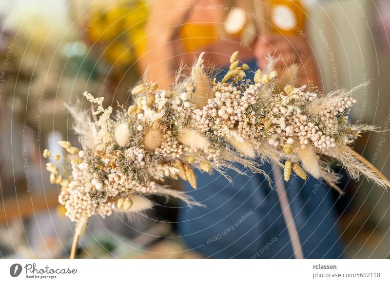 Nahaufnahme eines Trockenblumenkranzes, der von einer Person in einer blauen Schürze gehalten wird, unscharfer Hintergrund Kranz aus Trockenblumen Person mit