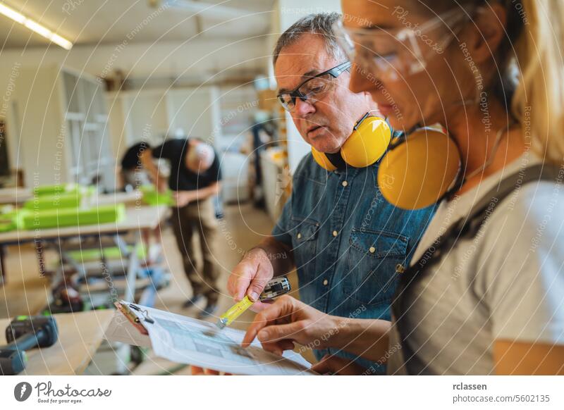 Zwei Zimmerleute prüfen einen Bauplan, während ein anderer im Hintergrund arbeitet professioneller Handwerker Teamwork Hobelbank Möbelindustrie Arbeiter