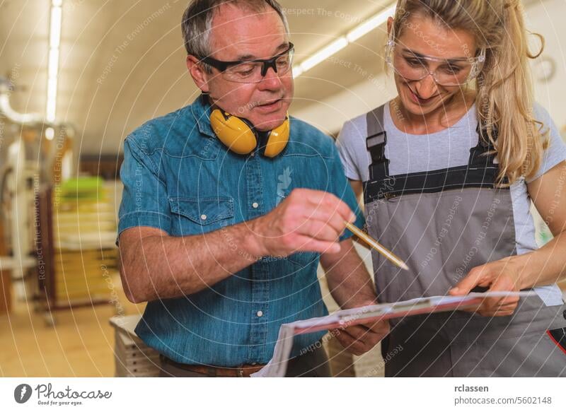 Mann und Frau bei der Durchsicht eines Dokuments in einer Schreinerei professioneller Handwerker Möbelindustrie Tischlerwerkstatt Überprüfungsdokument