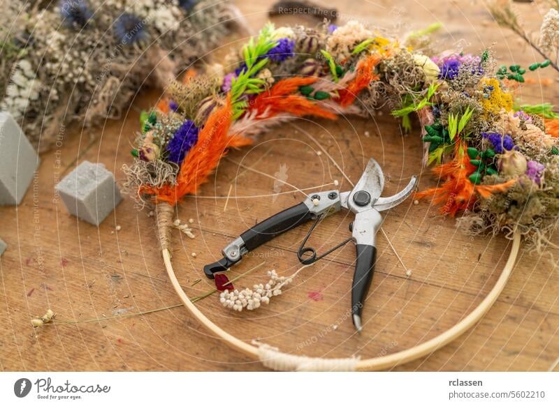 Draufsicht auf einen bunten Trockenblumenkranz, der mit einer Floristenschere auf einem Holztisch bearbeitet wird Ansicht von oben Kranz aus Trockenblumen