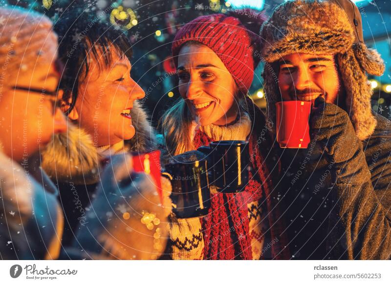 Freunde trinken Glühwein auf einem Weihnachtsmarkt Bowle Frohe Weihnachten Tasse Kakao Handschuhe traditionell Deutsch Schneeflocken Feiertag Bokeh