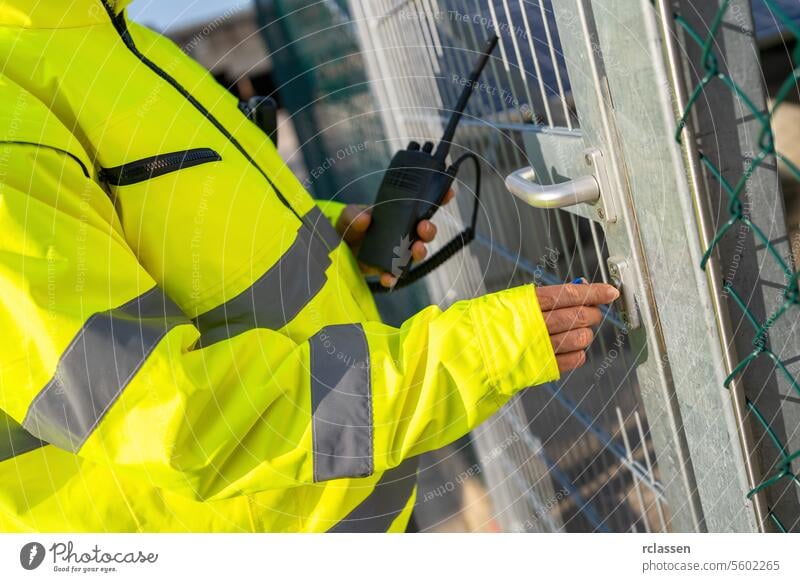 Nahaufnahme eines Arbeiters mit einem Walkie-Talkie, der ein Metalltor öffnet Funkgerät Eröffnung Warnschutzjacke Sicherheit Mitteilung Zugang manuell im Freien