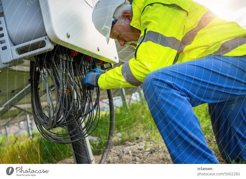 Ingenieur an einer Verteilerstation in einem Solarmodulpark, der mit Kabeln hantiert. Alternative Energie ökologisches Konzept Bild. Elektrizität Arbeiter