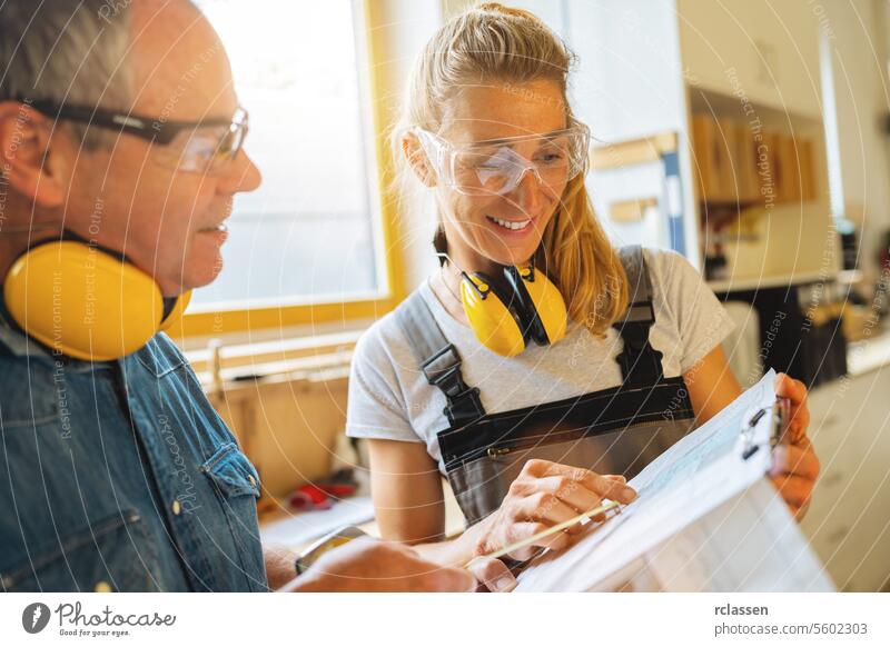 glückliche Zimmerleute, die in einer Tischlerei einen Bauplan prüfen professioneller Handwerker Teamwork Hobelbank Möbelindustrie Arbeiter Schreinerei