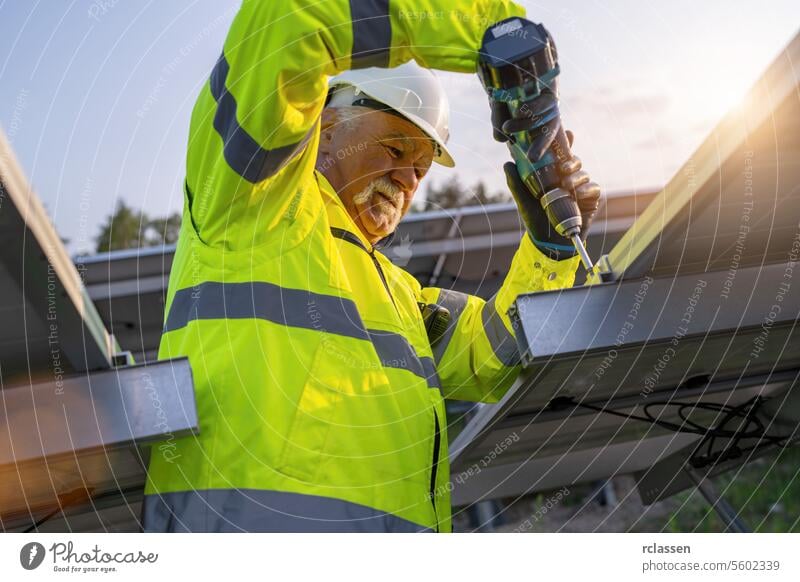 Ingenieur mit einem Akkubohrer zur Installation von Sonnenkollektoren in der Morgendämmerung. Alternative Energie ökologisches Konzept Bild. Meisteringenieur