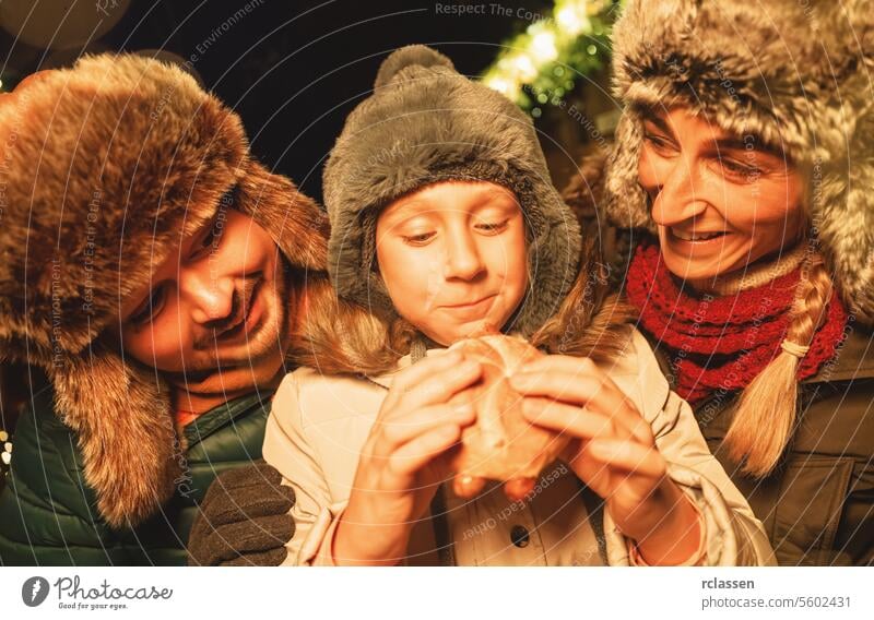 Familie beim Essen auf einem Weihnachtsmarkt, Kind isst mit Freude ein Wurstbrot freudig Frohe Weihnachten traditionell Glühwein Deutsch Weihnachtsbaum