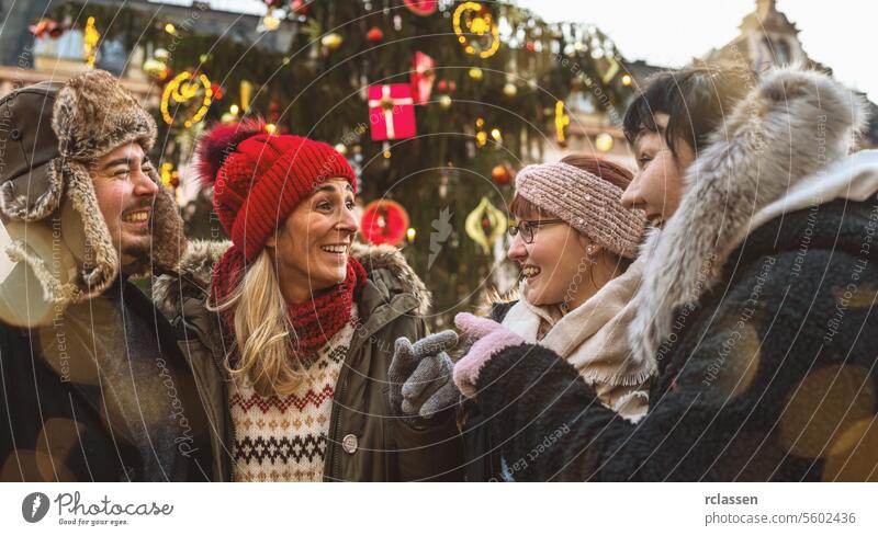 Weihnachtsmarkt für eine Gruppe von Freundinnen, die vor einem geschmückten Baum heißen Glühwein trinken Neujahr Weihnachten Lebensmittel Treffpunkt Winter Frau