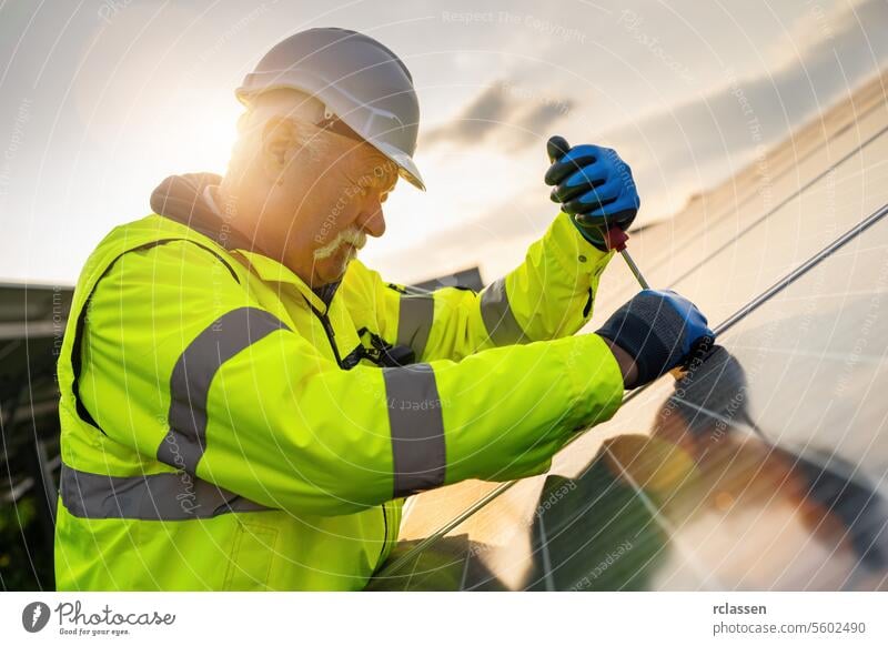 Ingenieur mit einem Schraubenzieher zu montieren ein Solarpanel in einem Solarpark bei Sonnenuntergang. Alternative Energie ökologisches Konzept Bild.