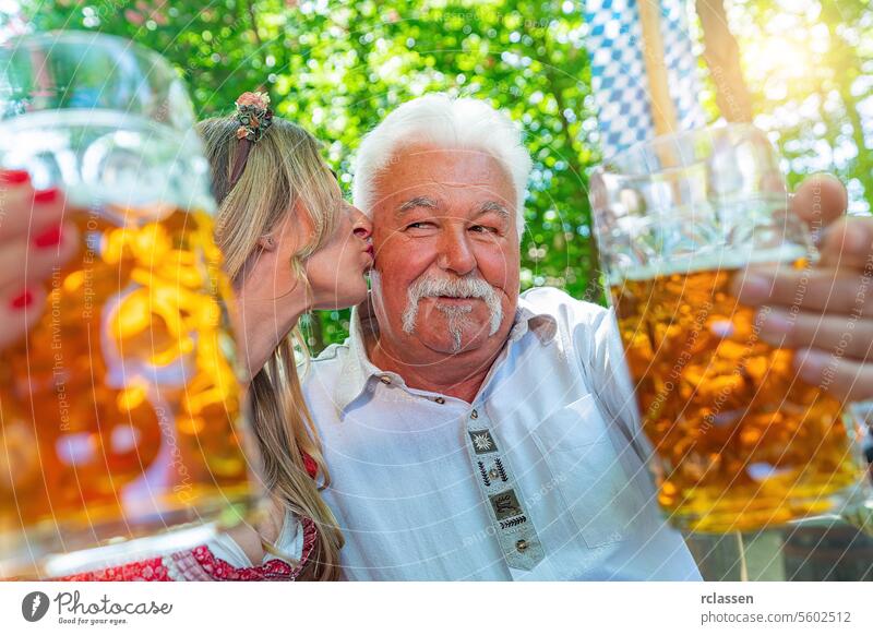 Tochter gibt ihrem Vater einen Kuss auf die Wange und sagt Prost oder stößt mit einem Krug Bier im bayerischen Biergarten oder auf dem Oktoberfest an Rentnerin