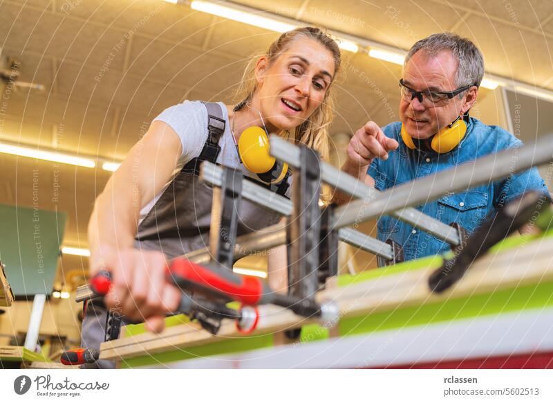 Auszubildender und Ausbilder bei der Arbeit mit Zwingen und Holz in einer hellen Werkstatt professionell Kunsthandwerker Hobelbank Möbelindustrie Arbeiter