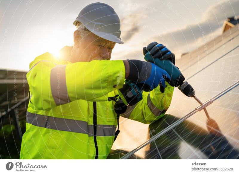 Ingenieur mit einem Bohrer für Solarpanel-Installation bei Sonnenaufgang. Alternative Energie ökologisches Konzept Bild. Technik & Technologie Pflanze Industrie