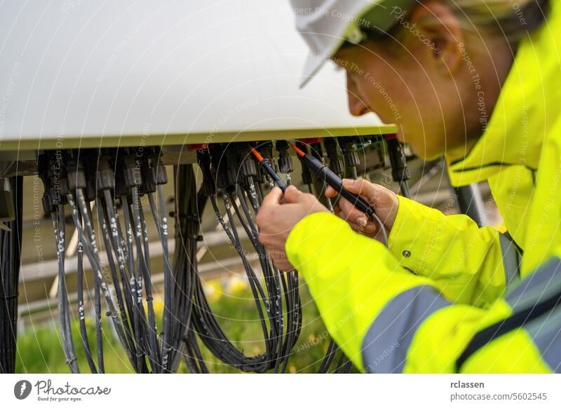 Techniker, der einen Spannungsprüfer am Stromverteilerkasten eines Solarfelds benutzt. Alternative Energie ökologisches Konzept Bild. Technik & Technologie