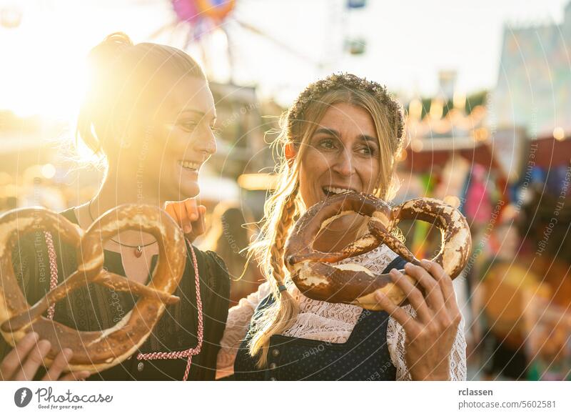 Freundinnen zusammen auf einer bayerischen Kirmes oder einem Oktoberfest oder in Tracht oder Dirndl eine Brezel oder Brezen essen Frau Party brezen biergarten