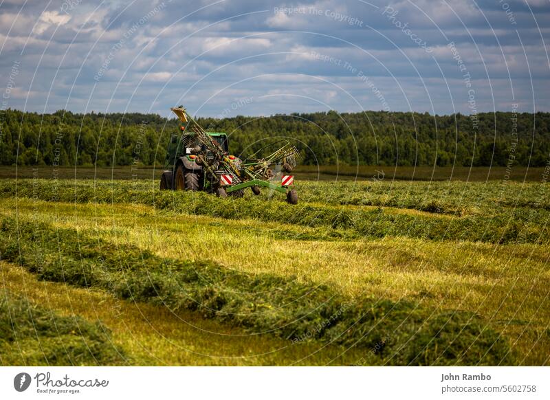 grüner Heutraktor auf einem Sommerfeld vor einem Gewitter - Teleobjektivaufnahme Wiese Land vorher Unwetter ländlich Licht landwirtschaftlich Tag Bauernhof Feld