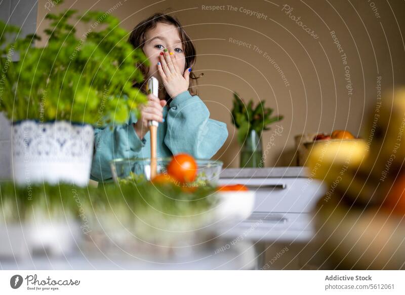 Grundschulkind bei der Zubereitung von Salat zu Hause Mädchen niedlich Fingernagel farbenfroh deckend Mund Hand Salatbeilage vorbereitend Küche Porträt