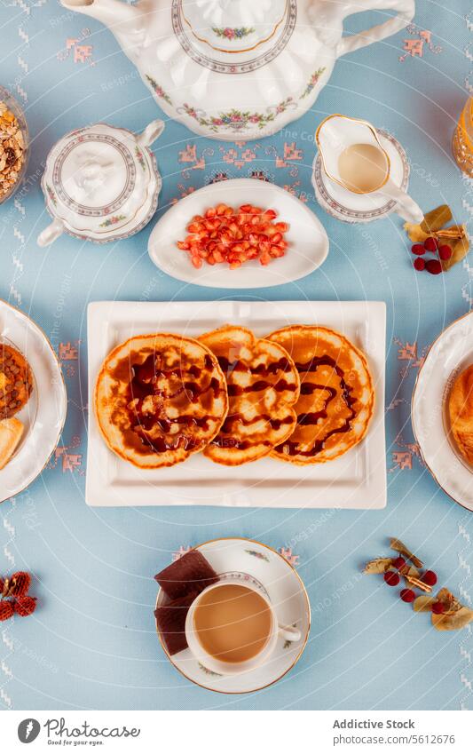 Elegantes Nachmittagstee-Setup mit Gebäck auf blauem Hintergrund Teekanne Porzellan Waffel süß Blauer Hintergrund Tischplatte Dessert Snack Teetasse Zucker