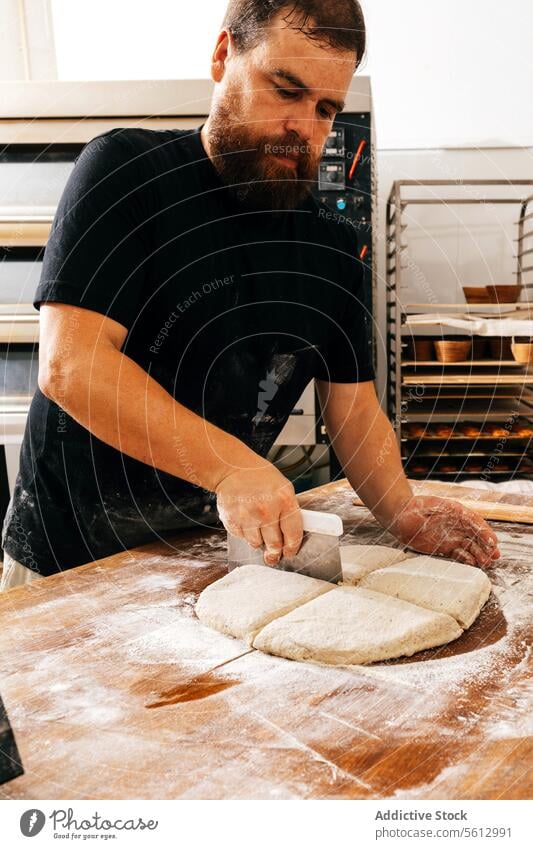 Küchenchef schneidet frischen Teig in der Bäckerei Koch Mann Schneiden Teigwaren Mehl Kutter Schaber Fokus ernst Vollbart Freizeitkleidung hölzern Tisch