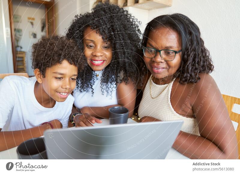 Frauen mit Teenagerjungen zu Hause Junge Laptop Kaffee Becher Lächeln Tisch Lifestyle Afro-Look Mutter Großmutter Sohn Tochter Enkel Sitzen heimwärts trinken