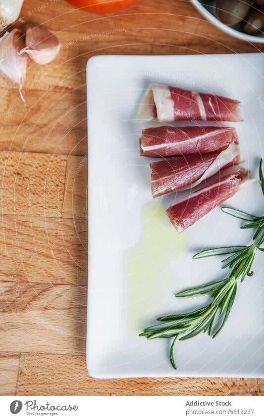 Scheiben von iberischem Schinken mit Rosmarin und Olivenöl Prosciutto weiße Platte Knoblauch aufgeschnitten Räucherschinken frisch Tomate Hintergrund